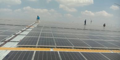 Workers inspecting a large field of solar panels under a cloudy sky.