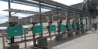 A row of green electrical inverters mounted outdoors under a metal canopy.