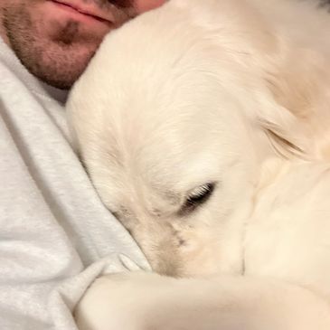 A person cuddling a calm white dog closely.