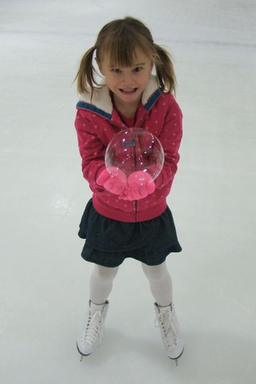 a little girl in ice skates holding a bubble