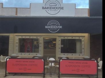 Front view of Modern's Bakehouse &amp; Eatery with outdoor seating and red barriers.