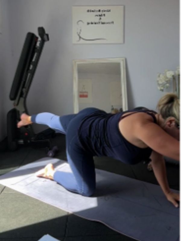 Woman in workout clothes doing a leg lift exercise on a yoga mat indoors.