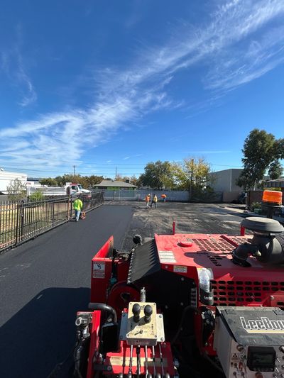 Workers paving a parking lot under a clear blue sky.