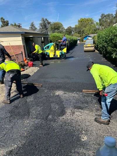 Workers repaving a driveway with asphalt using rollers and rakes.