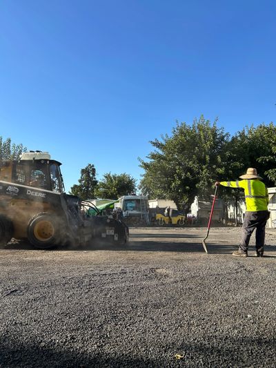Worker in yellow vest using a rake near construction machinery on gravel.
