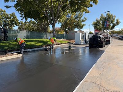 Workers smoothing freshly poured concrete on a sunny day.