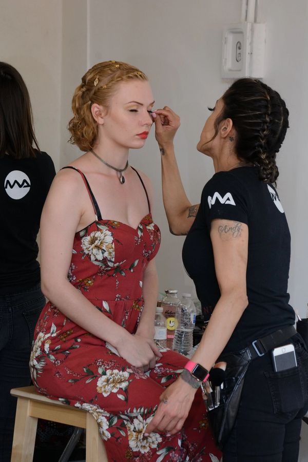A makeup artist applies makeup to a woman in a floral dress.