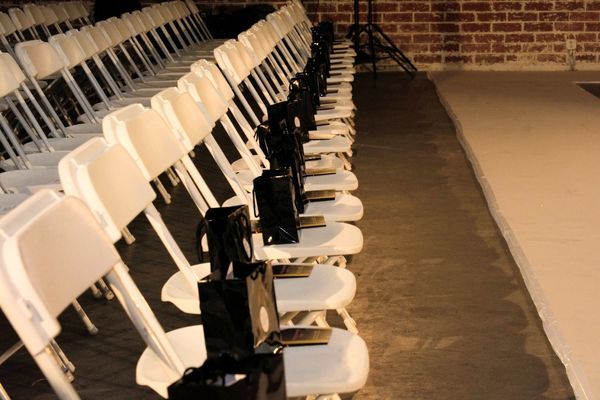 Rows of white chairs with black gift bags arranged for an event.