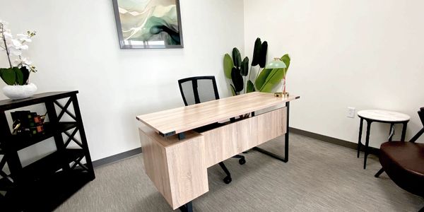 Minimalist office with a wooden desk, black chair, plants, and modern decor.