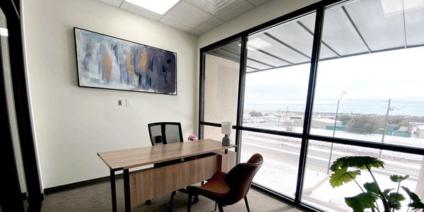 Modern office with large window, desk, and chairs overlooking a snowy street.