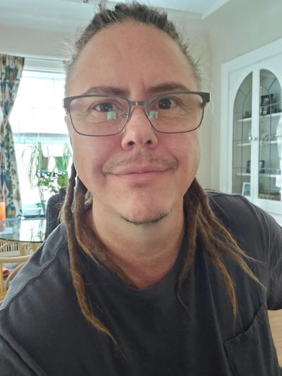 Man with glasses and dreadlocks smiling indoors.