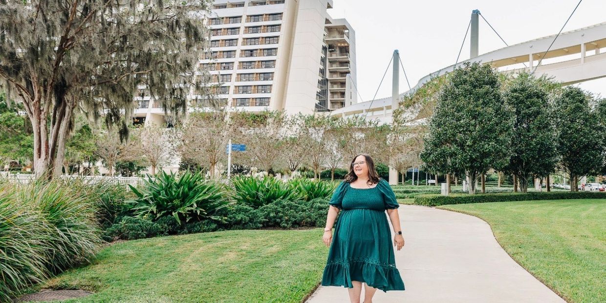 Woman in green dress walking on path near modern building and greenery.