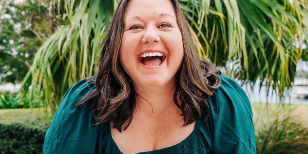 A joyful woman in a teal dress laughing outdoors with palm trees in the background.