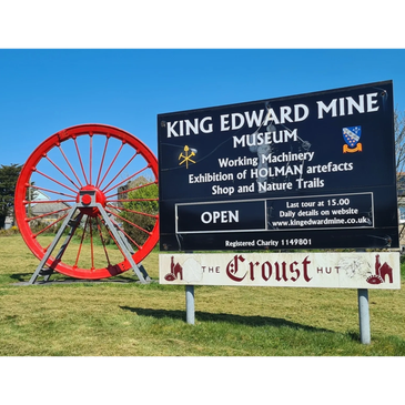 Signboard for King Edward Mine Museum with a large red wheel in the background.