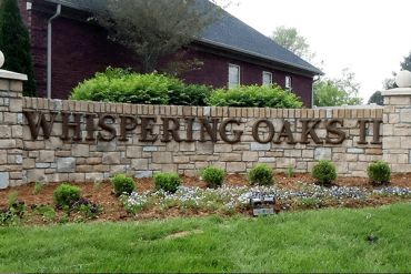 Stone sign for Whispering Oaks II with landscaping in front.