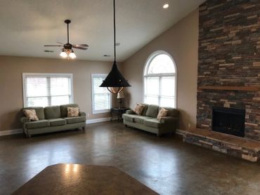 Spacious living room with two green sofas and a stone fireplace.