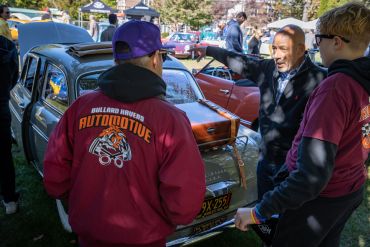 People discussing classic cars at an outdoor automotive event.