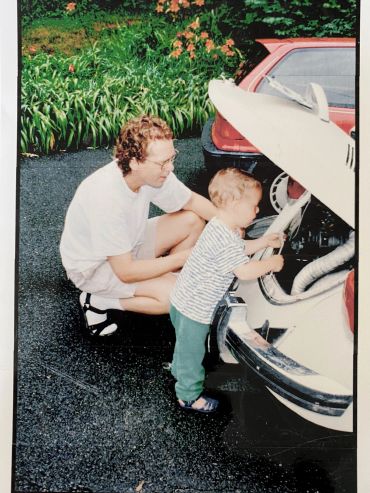 A man and child explore the trunk of a vintage white car outdoors.