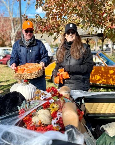Two people in fall hats and jackets holding baskets with autumn decorations.