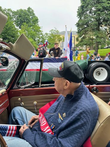 An elderly veteran rides in a convertible during a patriotic parade.