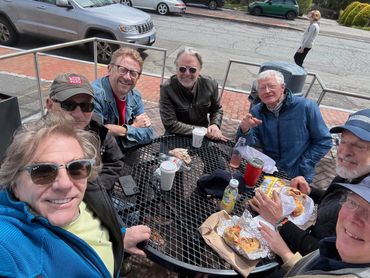 Group of friends enjoying a casual outdoor meal at a round metal table.