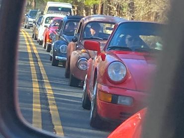 Classic cars lined up in a traffic jam, seen through a side mirror.