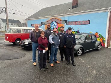 Mentors and Educators posing in front of vintage Volkswagen cars and a colorful mural. Mentors & Motors™