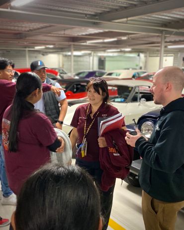 A group of people chatting in a vintage car garage.