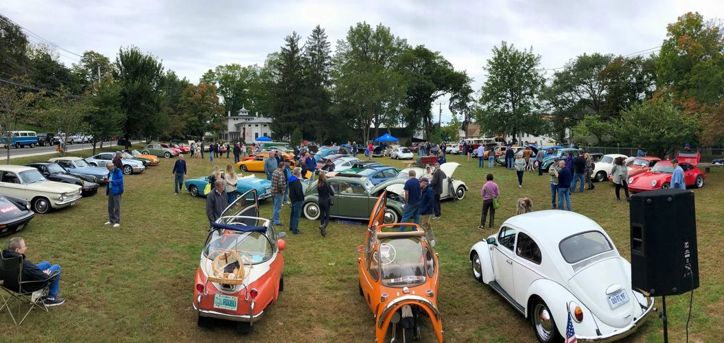 Classic car show with vintage and microcars on a grassy field attended by many people.