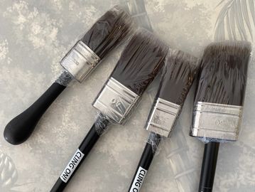 Four paintbrushes wrapped in plastic on a gray surface.