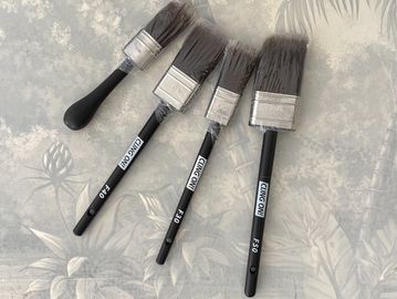 Four paintbrushes of different sizes arranged on a floral surface.
