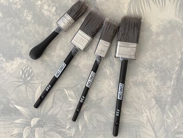 Four paintbrushes of different sizes arranged on a floral surface.