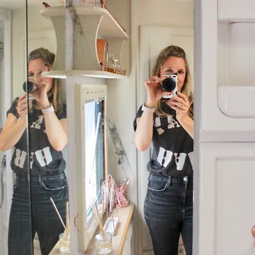 Woman taking a photo of herself in a mirror inside a bright room.