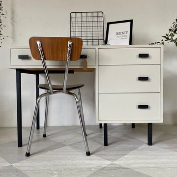 Minimalist desk setup with a wooden chair and white drawers.