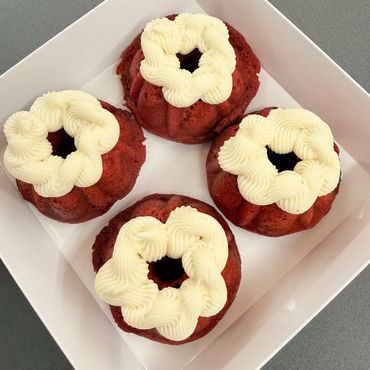 Four red velvet mini bundt cakes with white frosting in a white box.