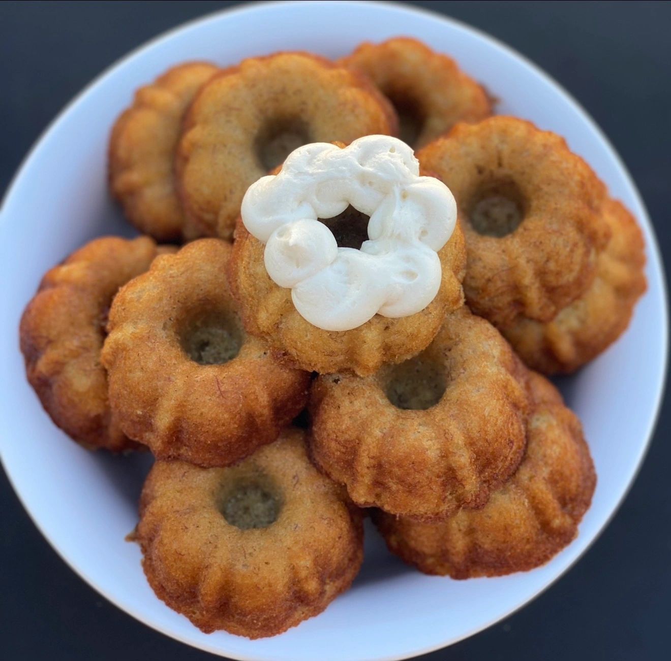 Mini bundt cakes stacked in a bowl with one topped with white frosting.