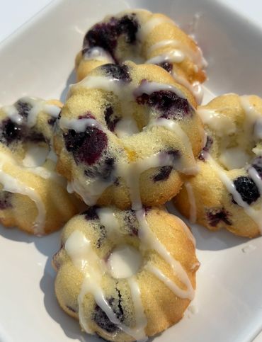 Mini blueberry bundt cakes drizzled with white icing on a white plate.