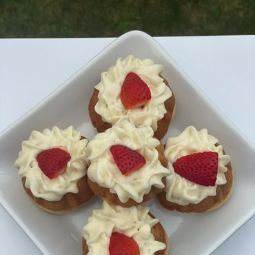 Five cupcakes with white frosting and a strawberry slice on top in a white dish.