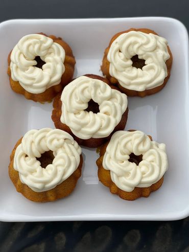 Five mini bundt cakes topped with swirls of creamy white frosting on a white plate.