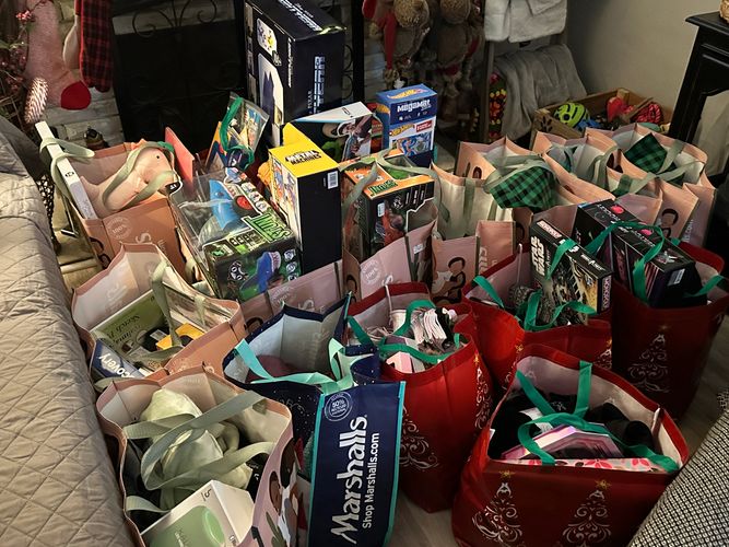 Multiple reusable shopping bags filled with toys and gifts on a living room floor.