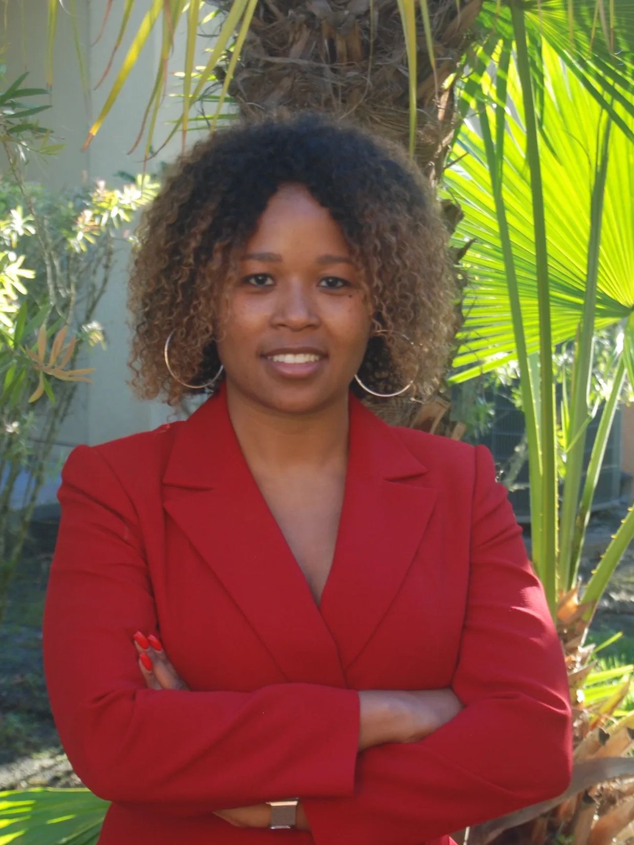 Stephanie standing in red suite with arms crossed, smiling  