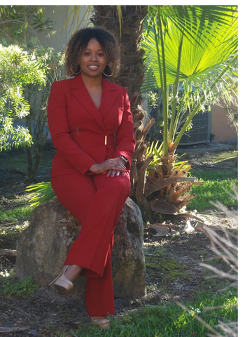 Stephanie sitting in a red suite and smiling with left leg crossed over right  in nude color heels