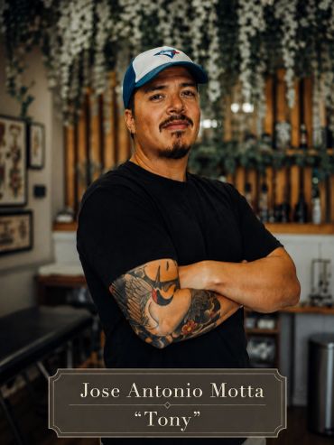 Man with tattooed arm and cap posing confidently.