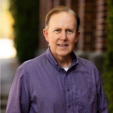 Man in purple shirt smiling outdoors.
