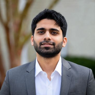 Man in gray suit smiling outdoors.