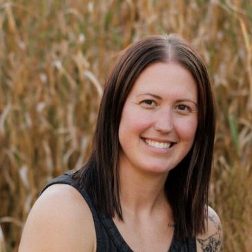 Smiling woman with brown hair outdoors in front of dry grass.