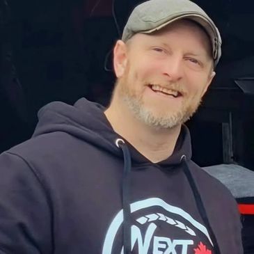 A smiling man wearing a cap and a hoodie with a logo.