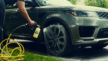 Person washing a Range Rover wheel with a foam sprayer.