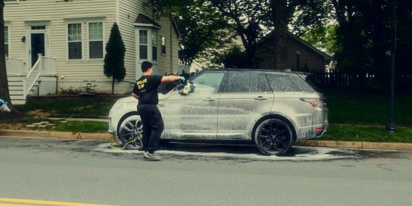 Professional car detailing – white SUV car wash with soap and foam on a suburban driveway.