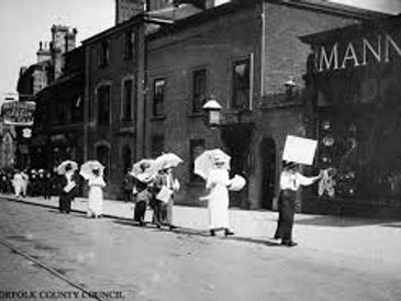 Early 20th-century suffragettes march with umbrellas and signs.
